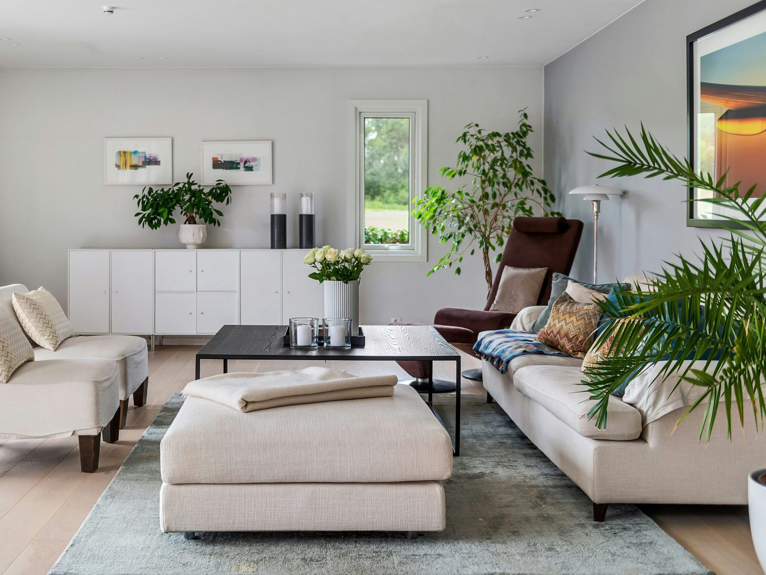 Modernes, freundlich gestaltetes Wohnzimmer mit hellen Möbeln und großen Pflanzen für ein harmonisches Raumgefühl.