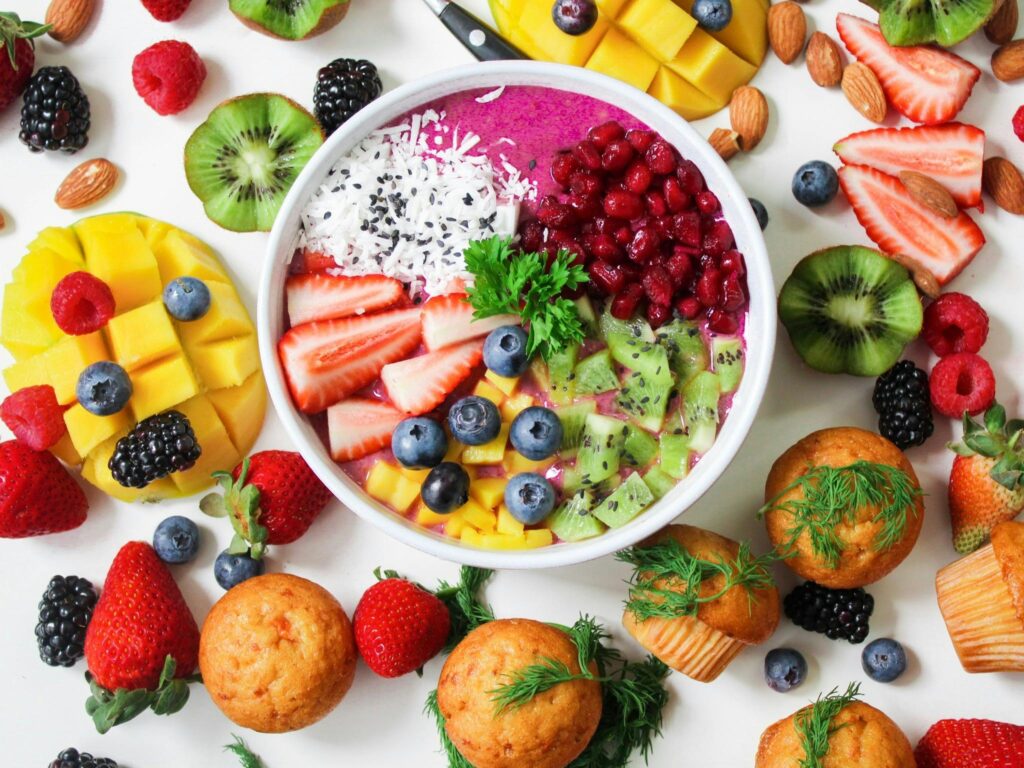 bunte Smoothie-Bowl mit frischem Obst, Nüssen, Samen und gesunden Muffins auf weißem Hintergrund