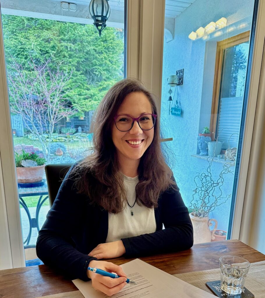 Ing. Tanja Hackl bei der Arbeit an einem Tisch sitzend und lächelnd.